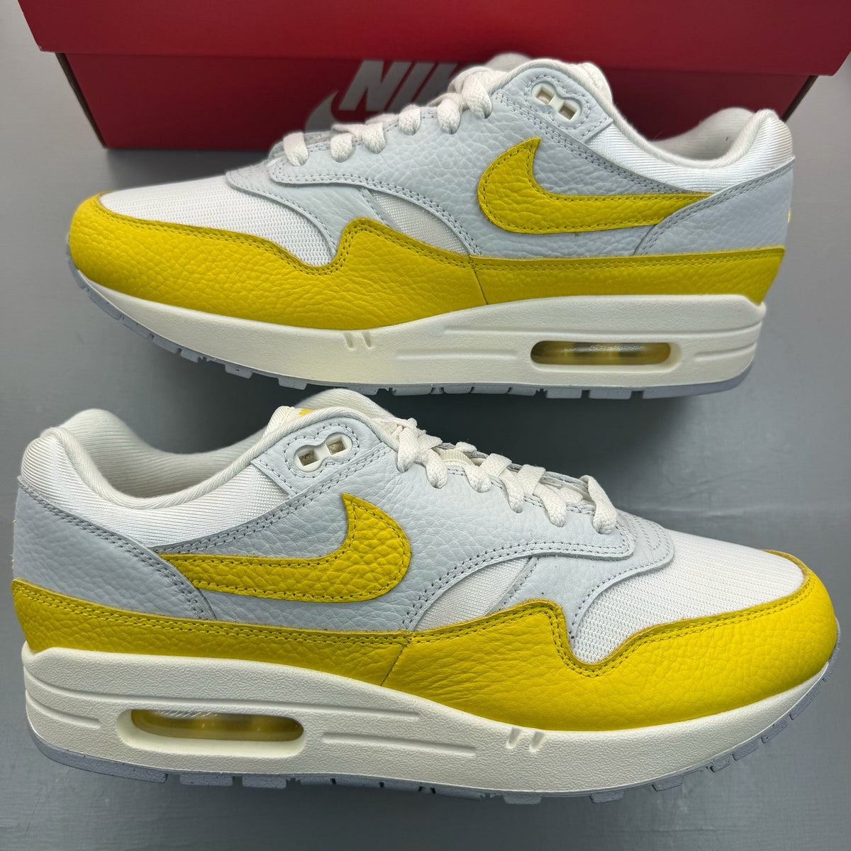Nike Air Max 1 white trainers with tour yellow accents and logo detail.