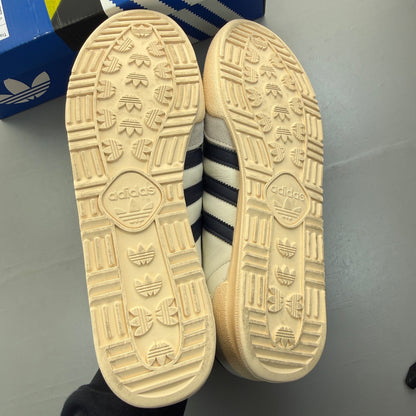 Adidas white trainers with navy accents and leather detailing, featuring iconic logo.
