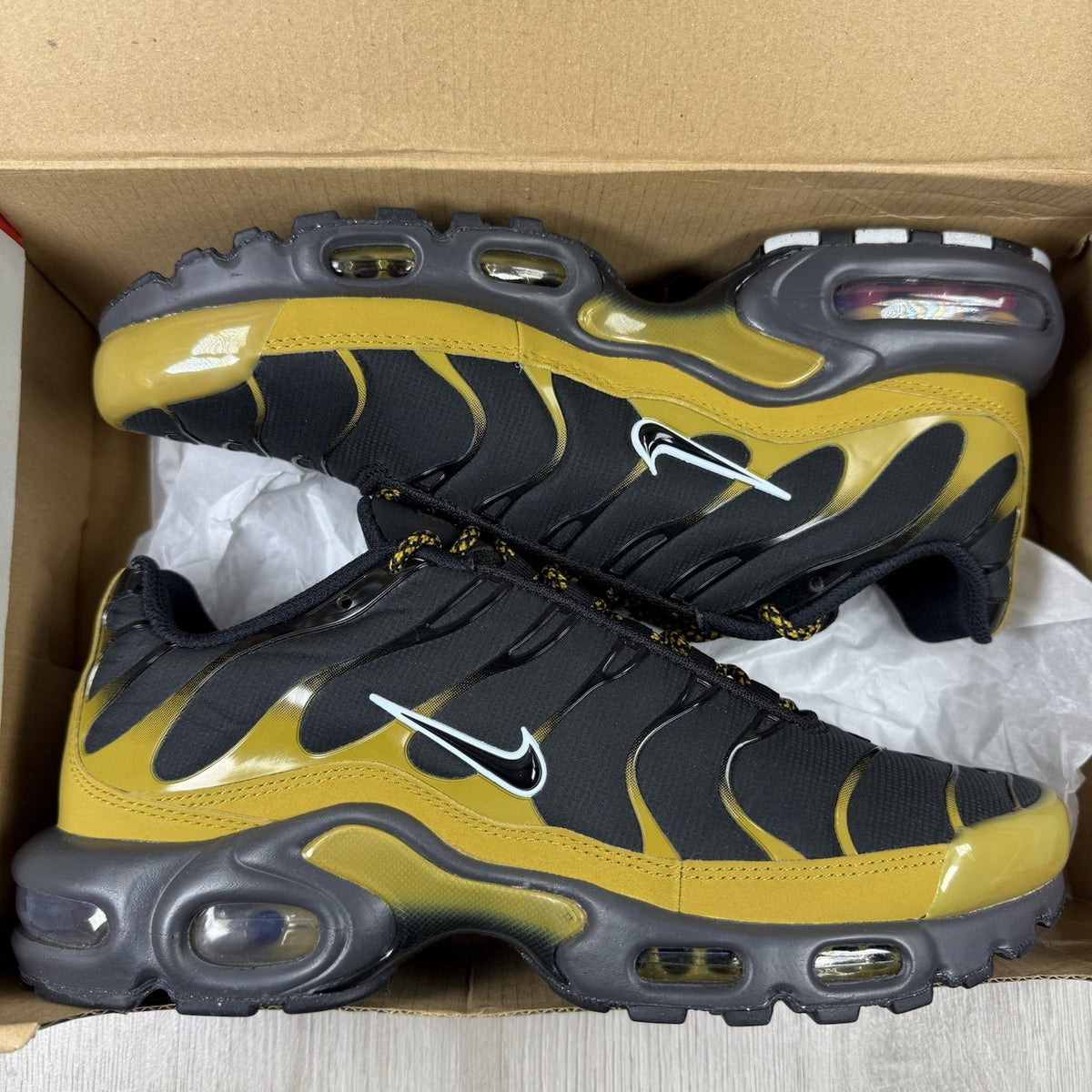 Nike Air Max Plus TN trainers black with gold accents and distinctive wavy pattern.