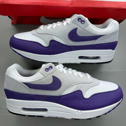 Nike Air Max 1 white trainers with purple accents and logo detail.