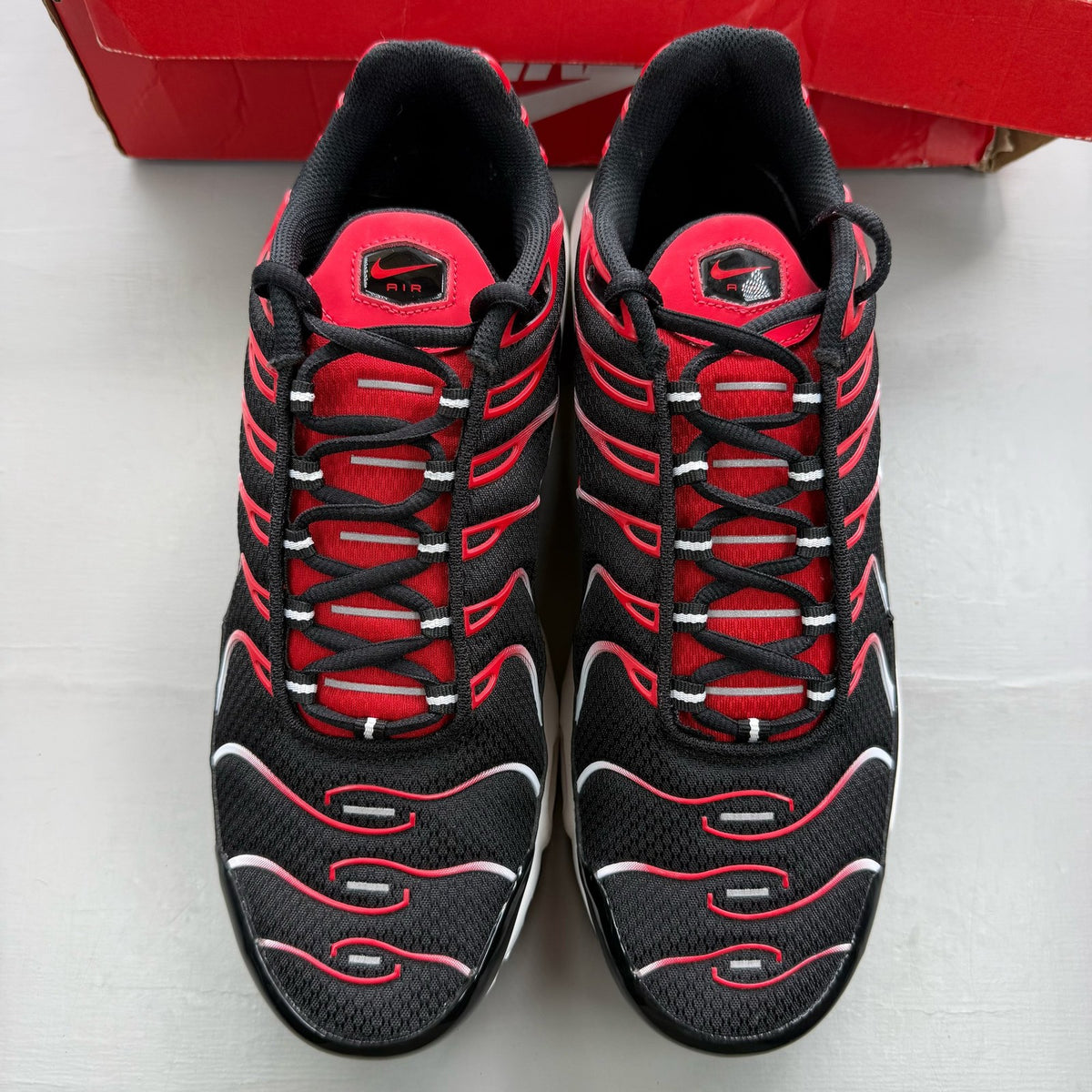 Nike Air Max Plus TN black trainers with white and university red accents, mesh material.