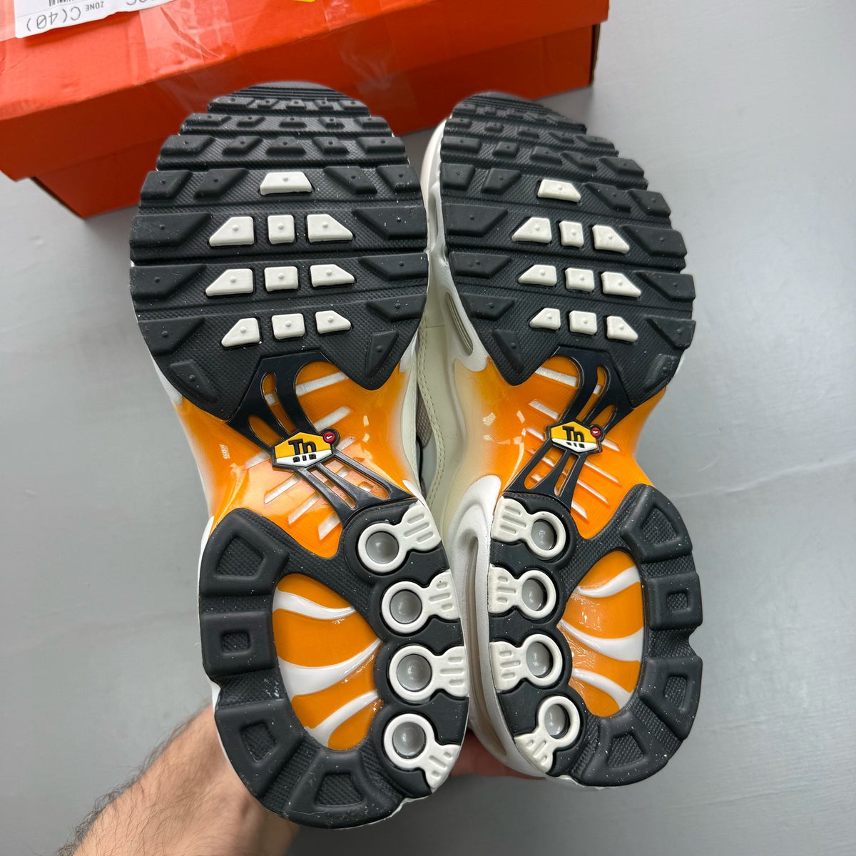 Nike Air Max Plus TN white trainers with orange accents and grey detailing.