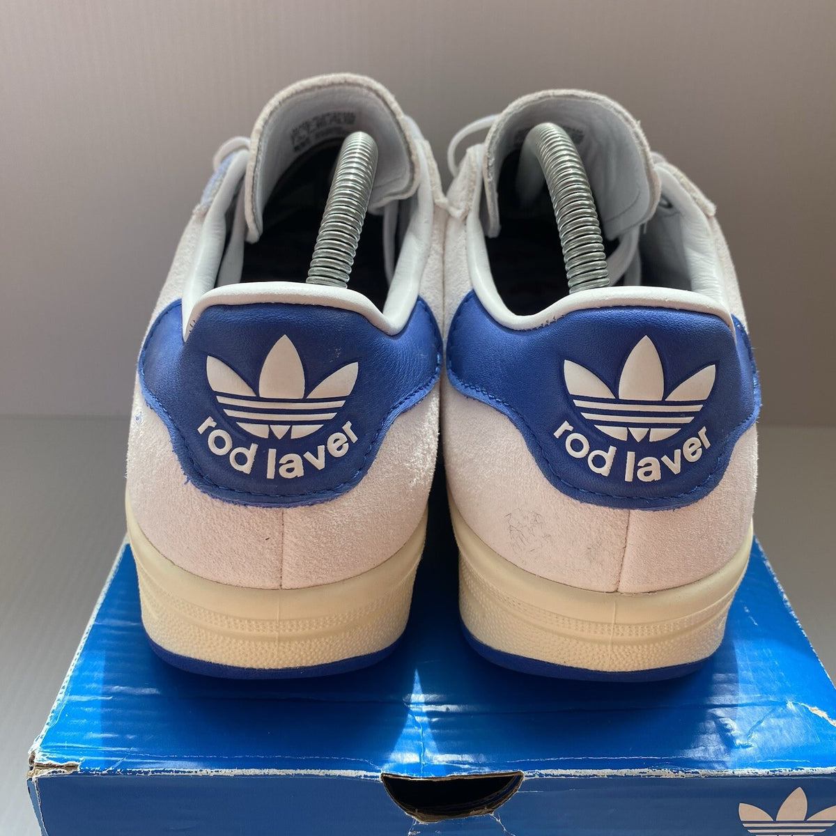 Adidas white trainers with blue and beige accents, featuring classic logo detail.