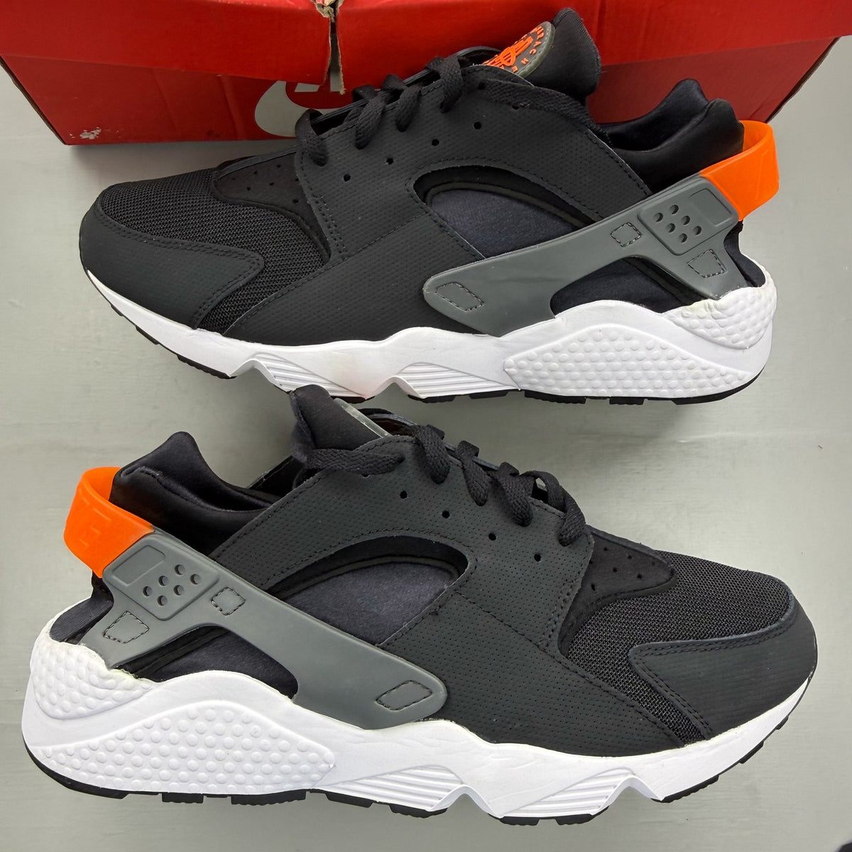 Nike black Air Huarache trainers with safety orange accents and white sole.
