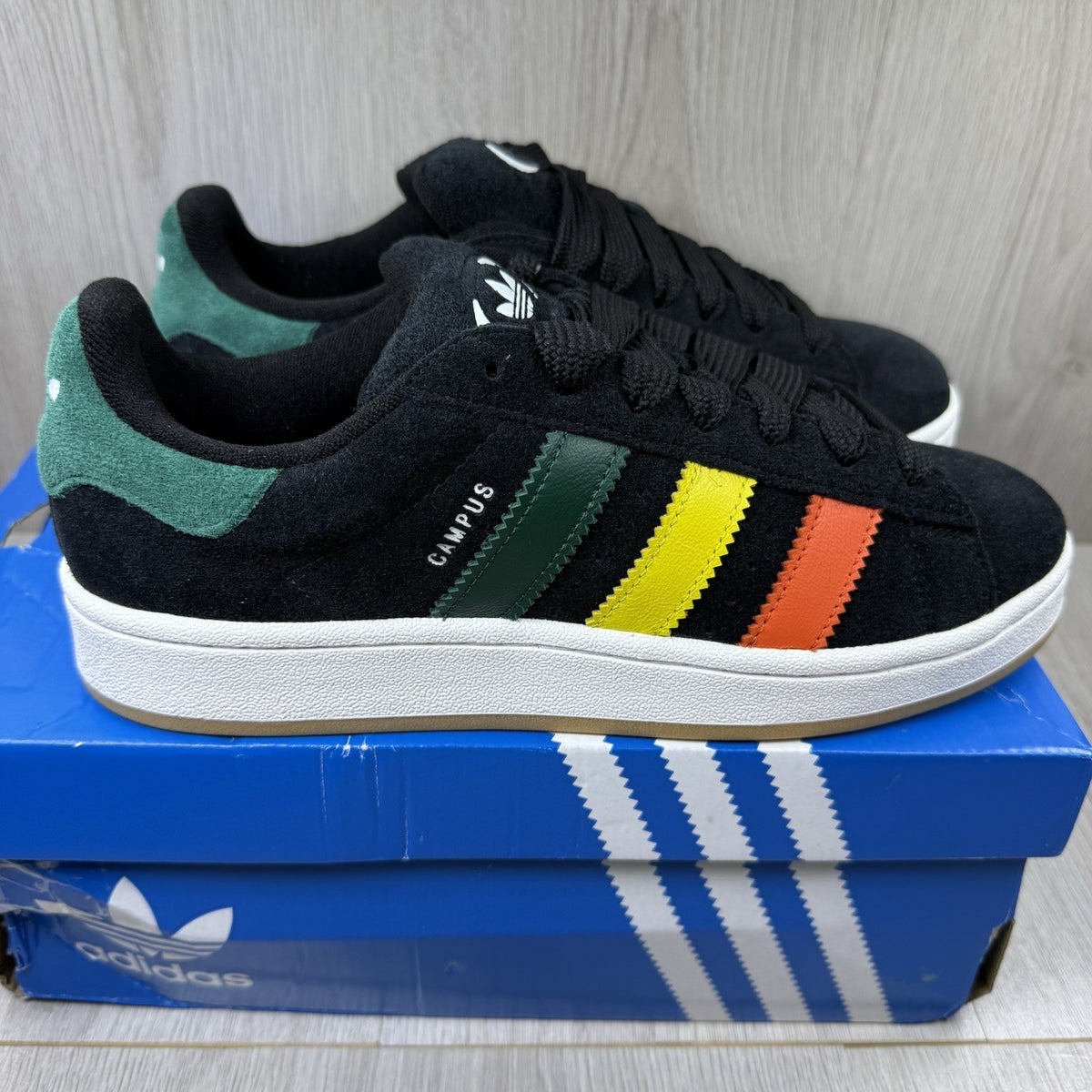 Adidas black trainers with yellow accents and classic three-stripe logo design.