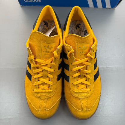 Adidas yellow trainers with black and gold accents, featuring iconic logo detail.