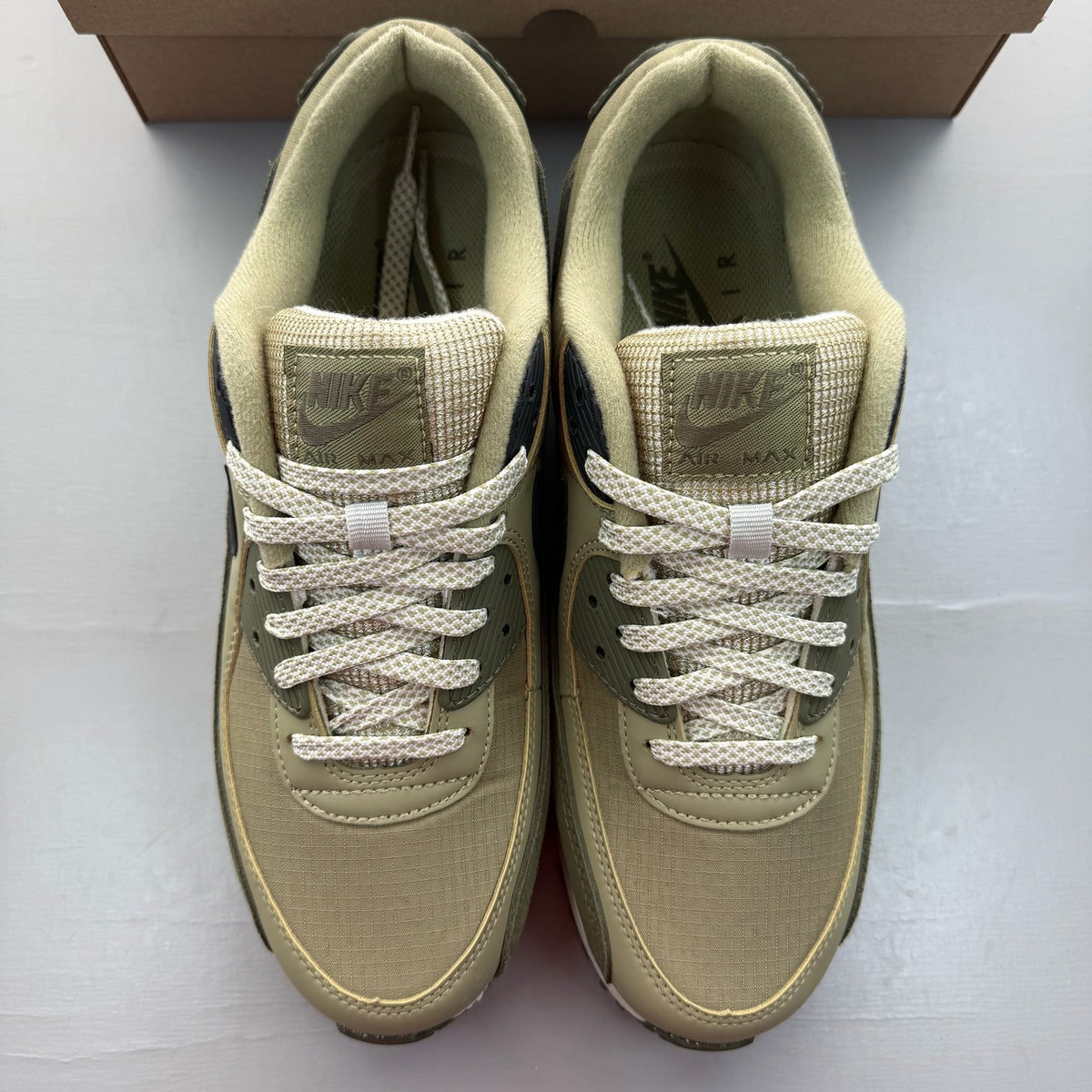 Nike Air Max 90 neutral olive green trainers with black accents and logo details.