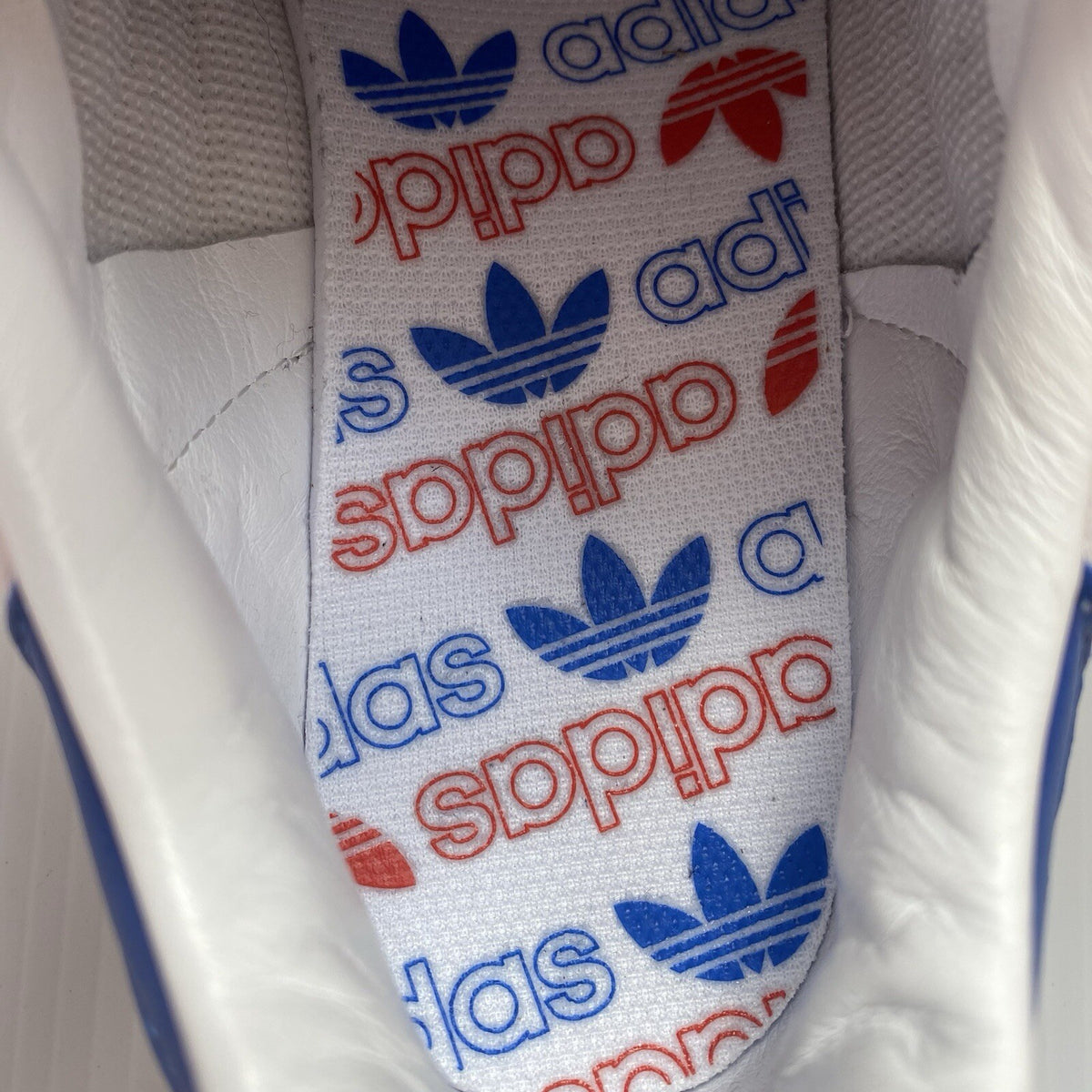 Adidas white trainers with blue and beige accents, featuring classic logo detail.