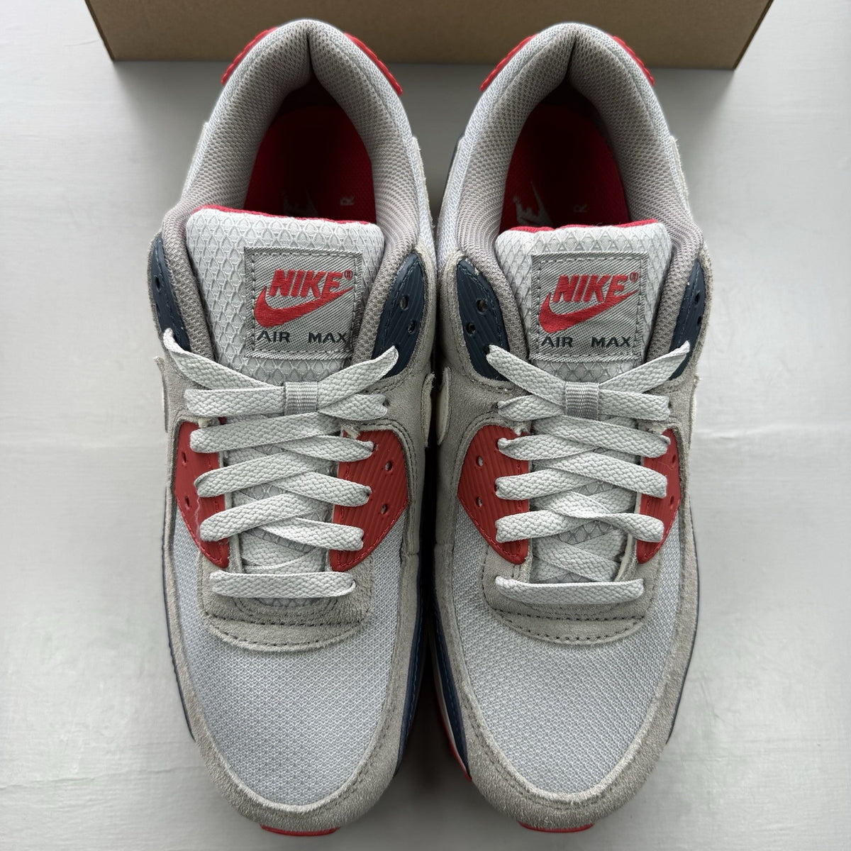 Nike Air Max 90 trainers white with red and navy accents, featuring logo details.