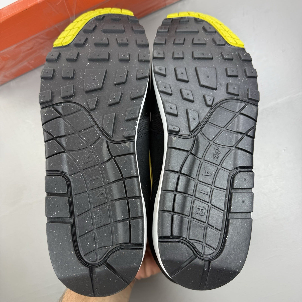 Nike Air Max 1 Essential black trainers with yellow accents and logo detail.