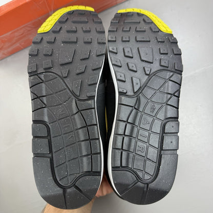 Nike Air Max 1 Essential black trainers with yellow accents and logo detail.