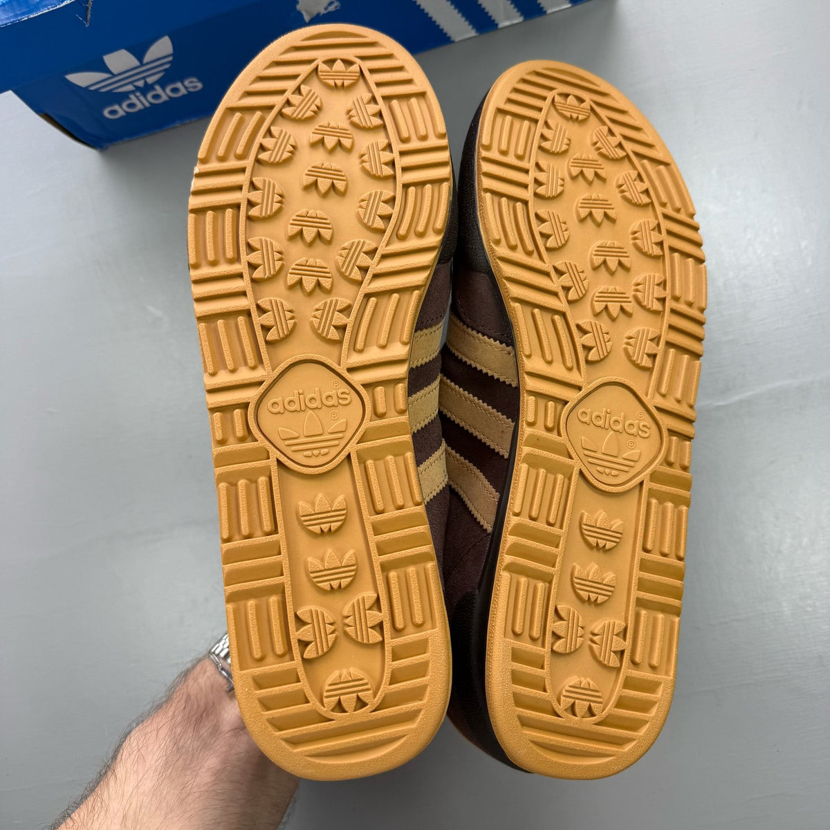 Adidas brown trainers with gold accents and gum sole, featuring iconic three stripes logo.