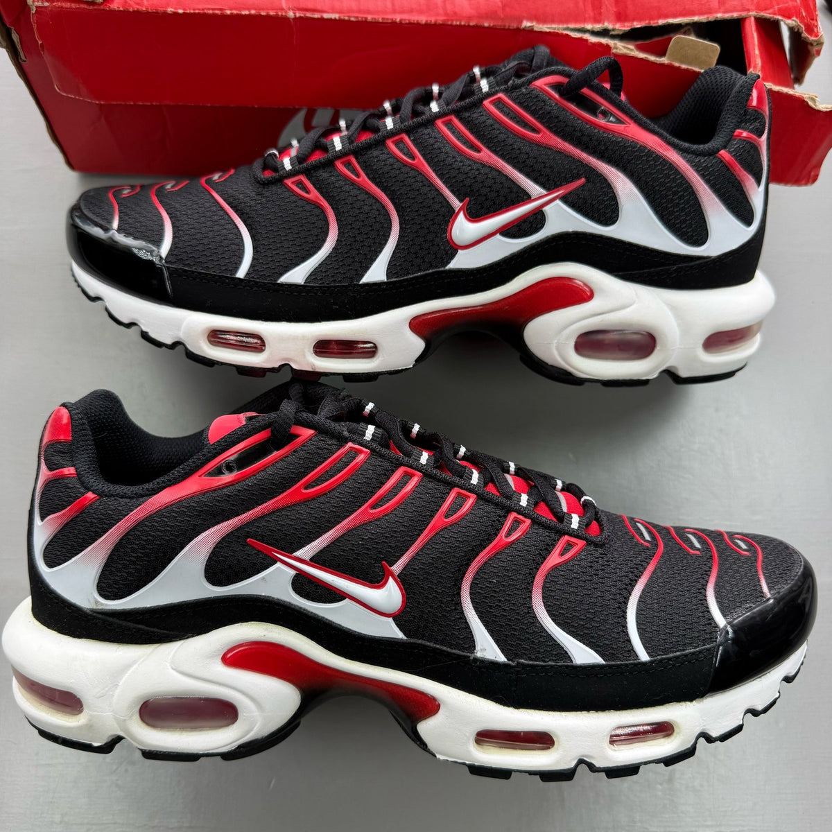 Nike Air Max Plus TN black trainers with white and university red accents, mesh material.