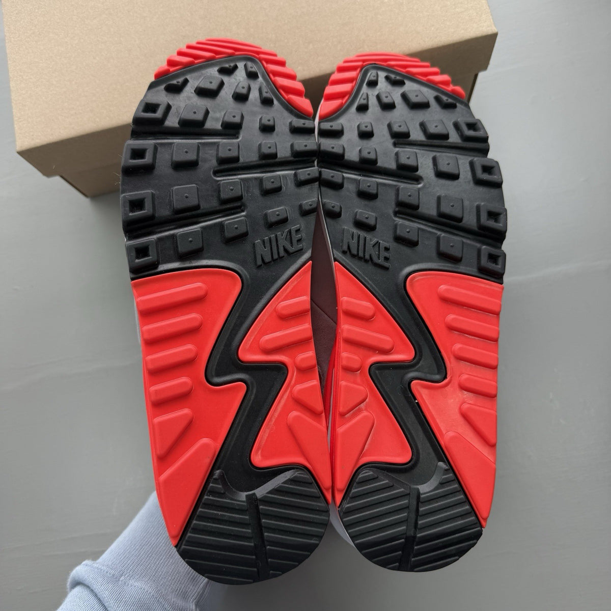 Nike Air Max 90 grey trainers with bright crimson accents and black detailing.