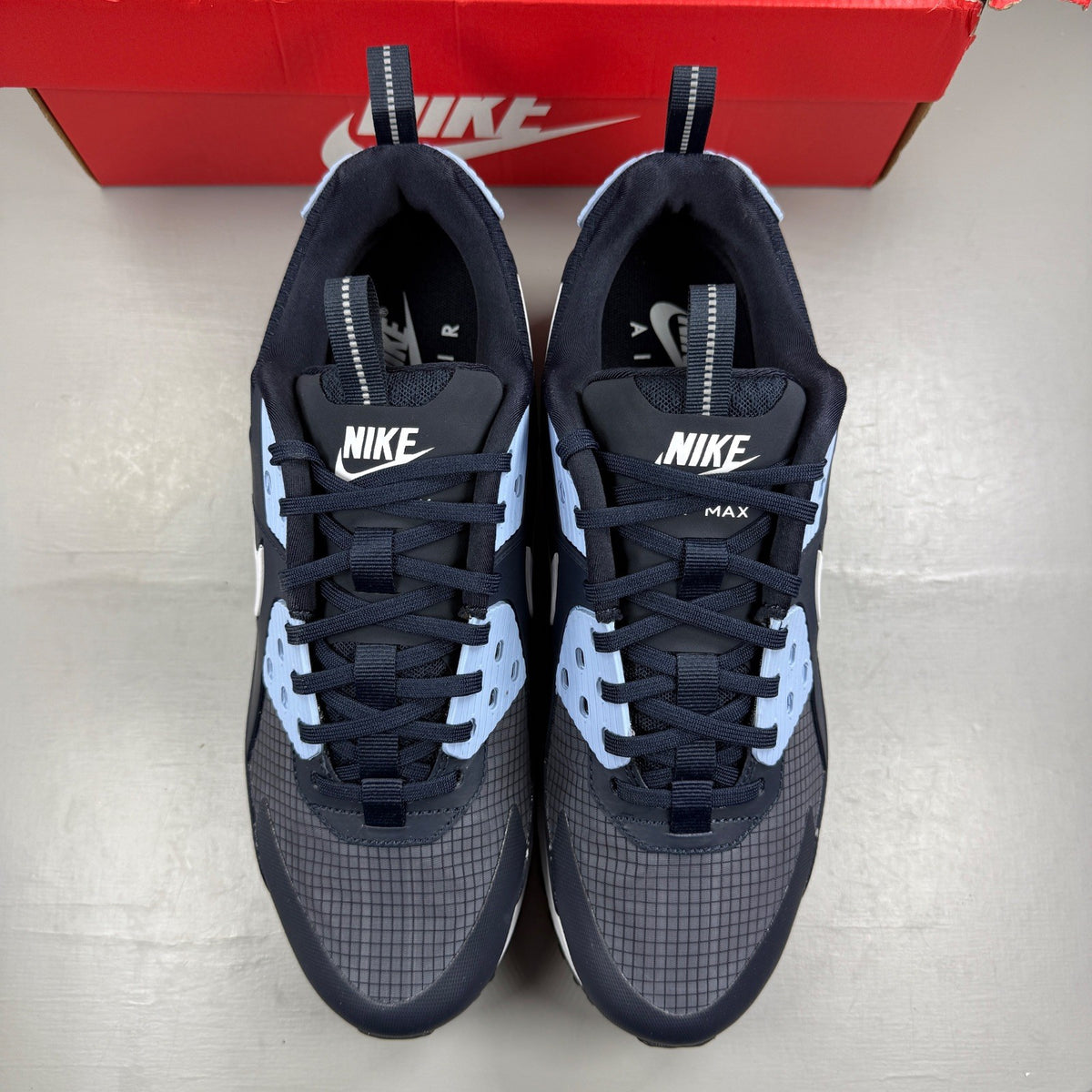 Nike Air Max 90 blue trainers with dark obsidian accents and signature swoosh logo.