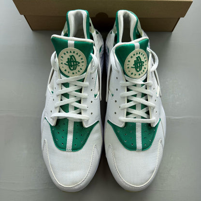 Nike Air Huarache white trainers with green accents and distinctive logo detailing.