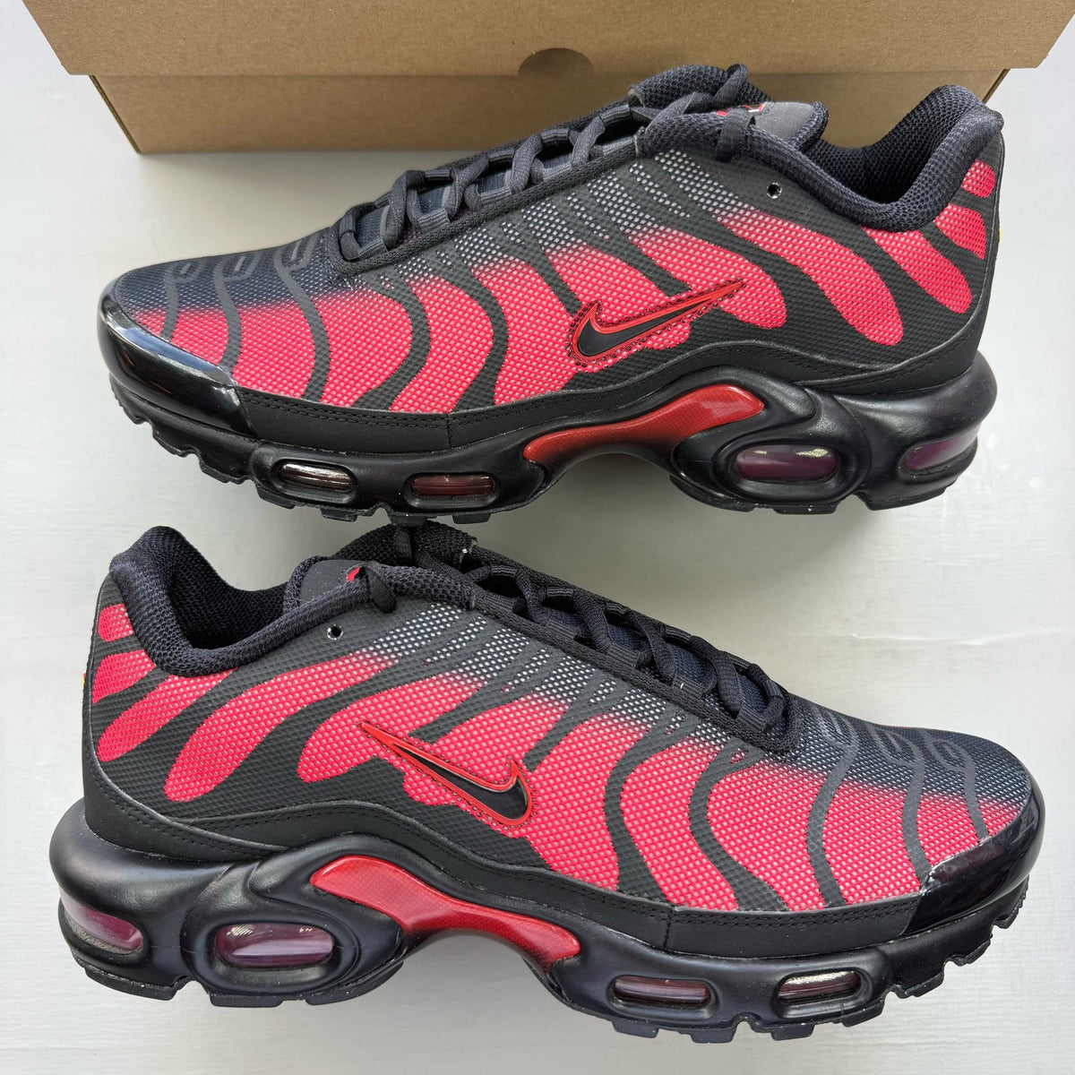 Nike black Air Max Plus TN trainers with reflective accents and red detailing.