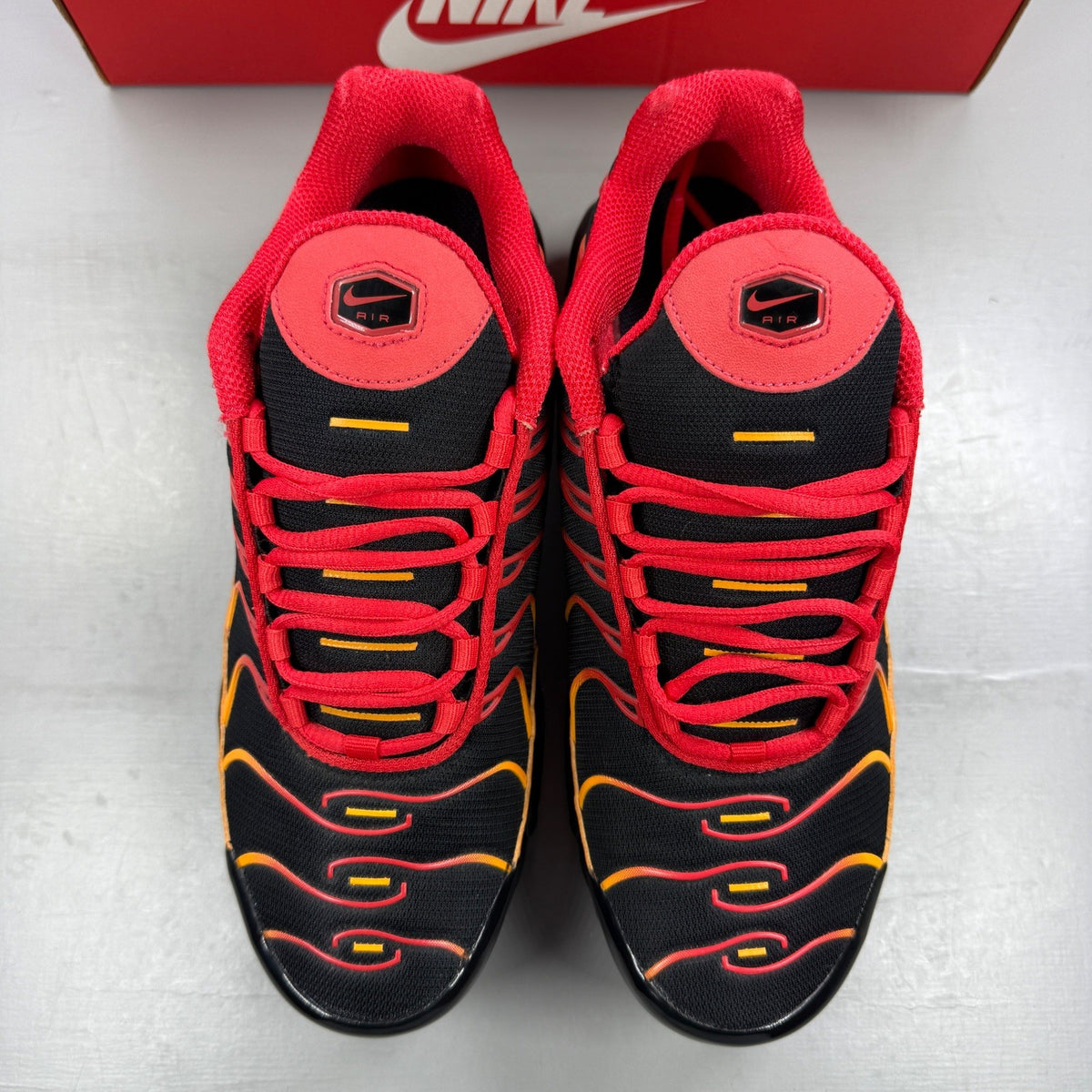 Nike black Air Max Plus TN trainers with red and orange accents and signature logo.