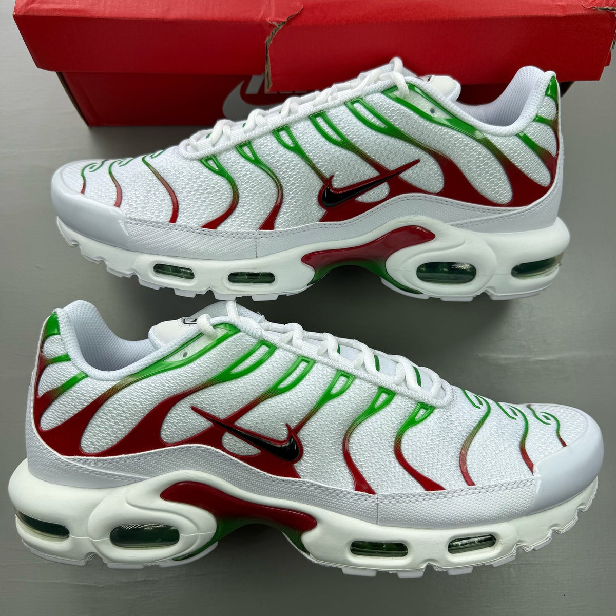 Nike Air Max Plus TN white trainers with green and red accents, featuring iconic logo.