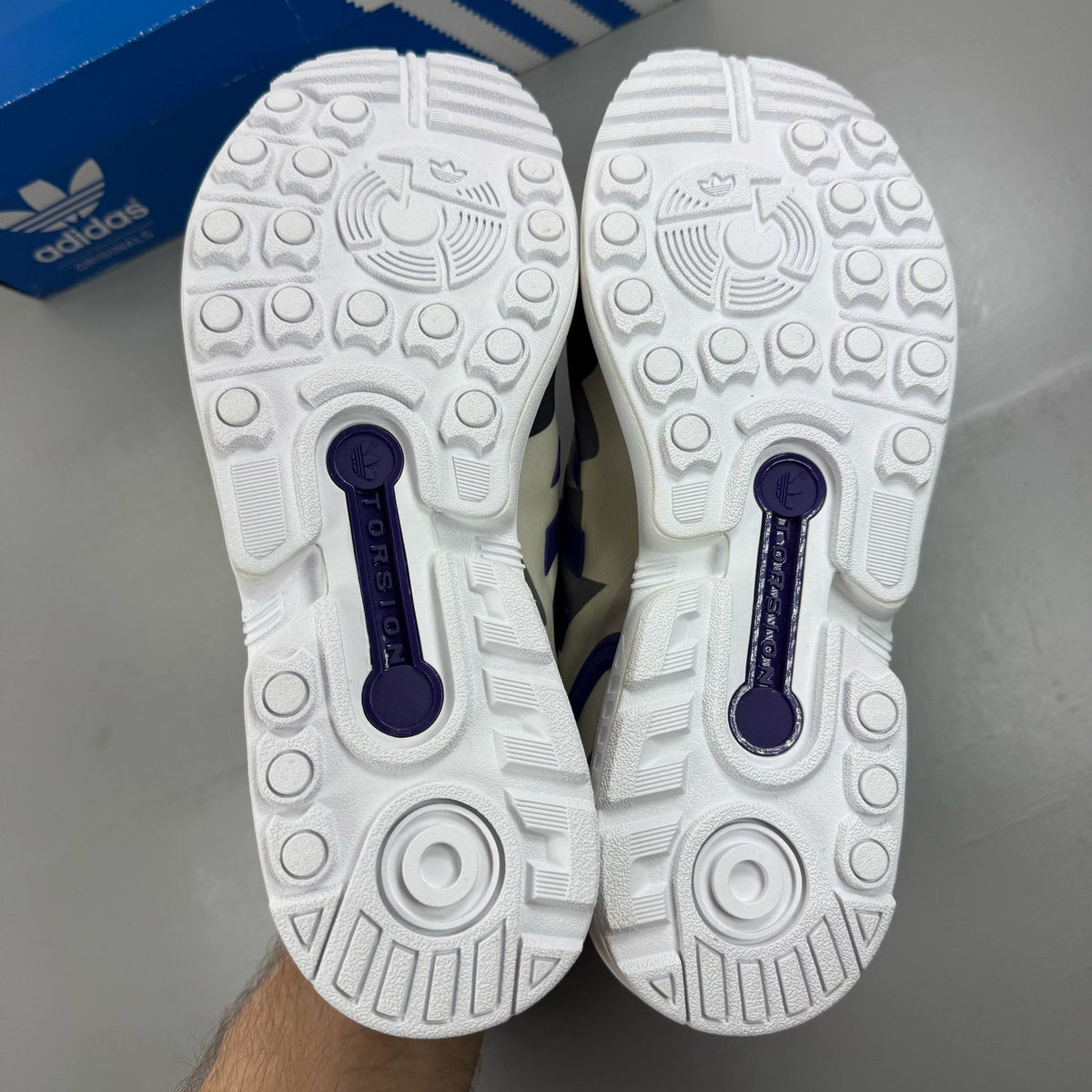 Adidas ZX Flux white trainers with purple and black accents, featuring iconic three-stripe logo.