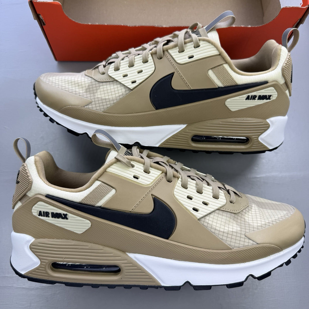 Nike Air Max 90 Drift beige trainers with white accents and logo detailing.