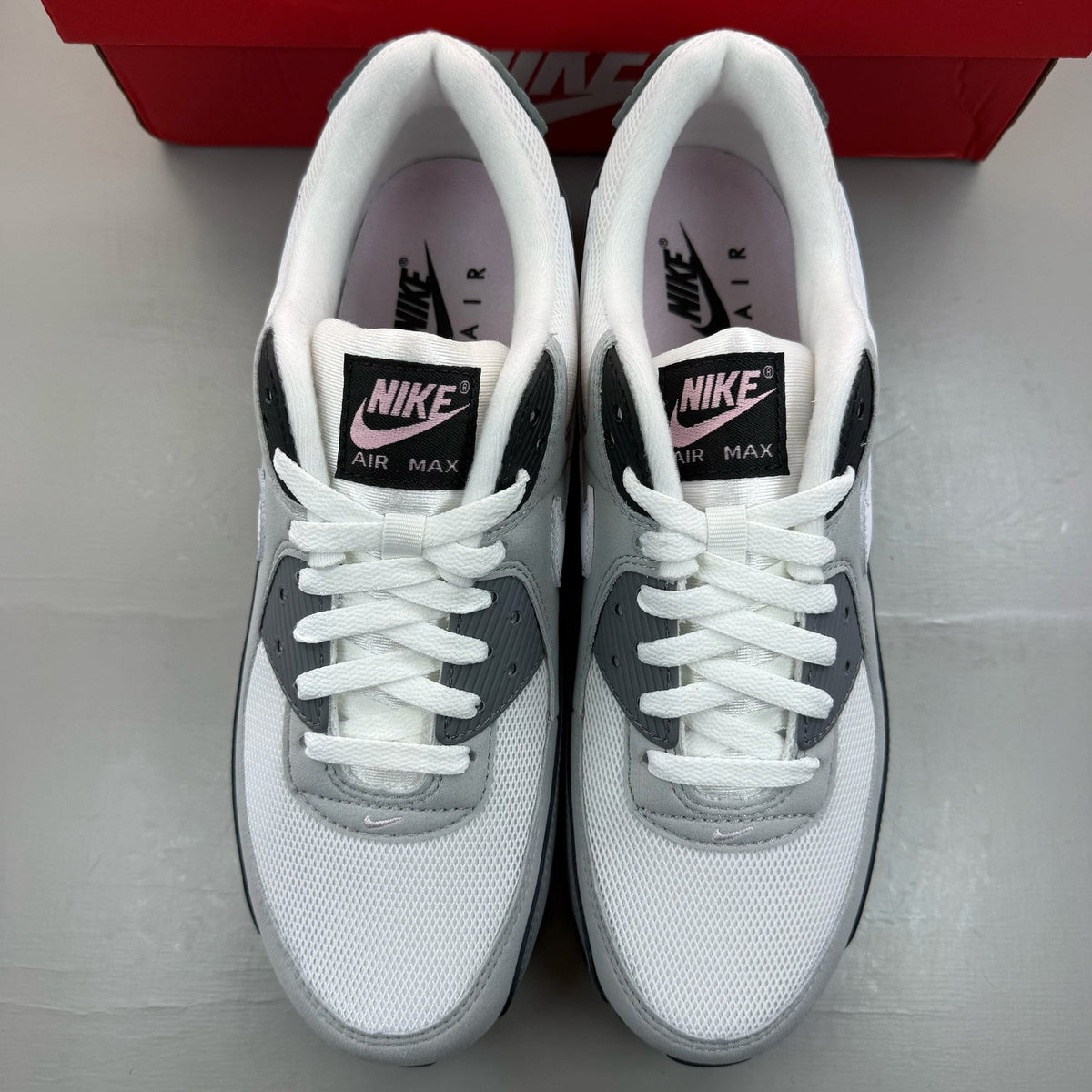 Nike Air Max 90 grey trainers with pink foam accents and white sole.