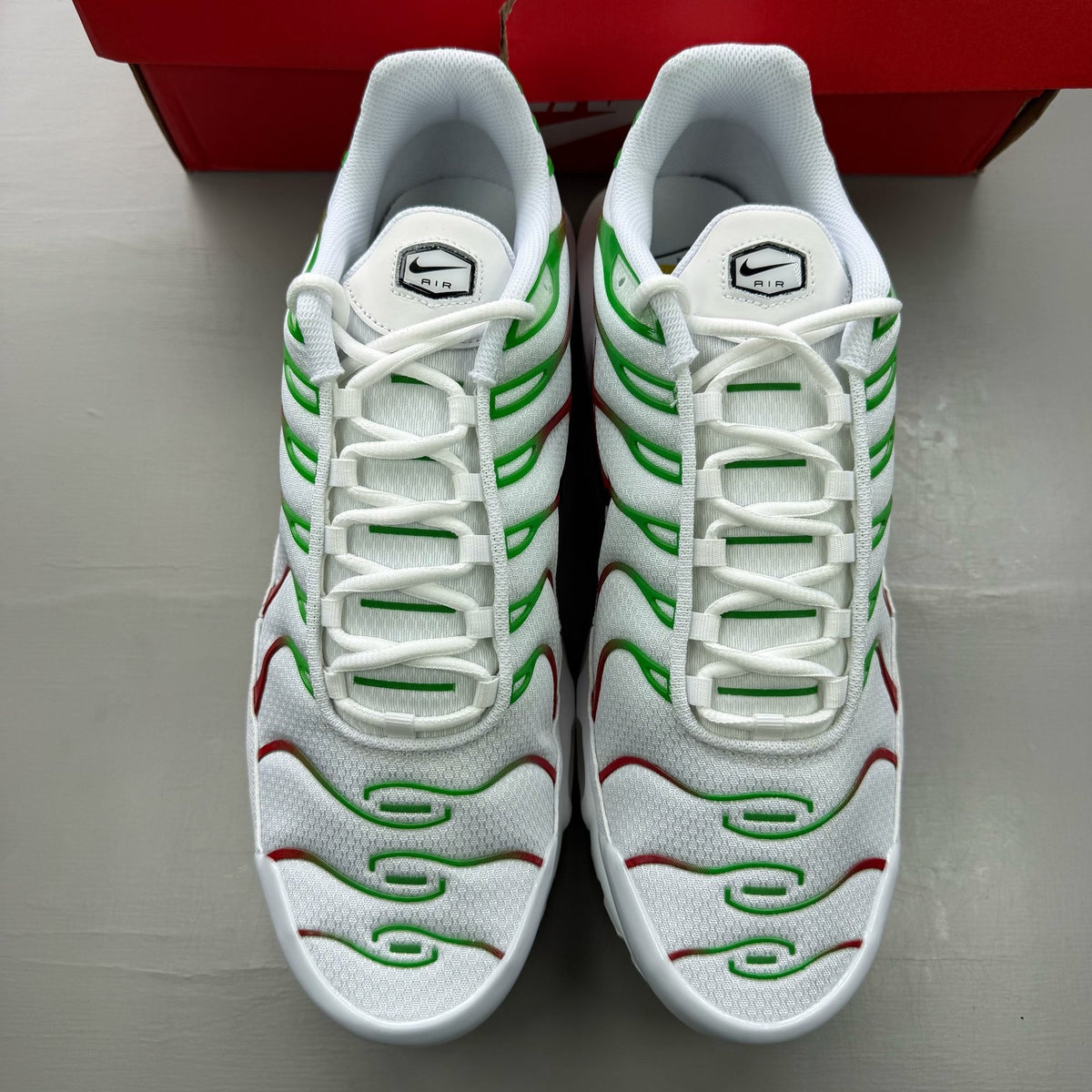 Nike Air Max Plus TN white trainers with green and red accents, featuring iconic logo.