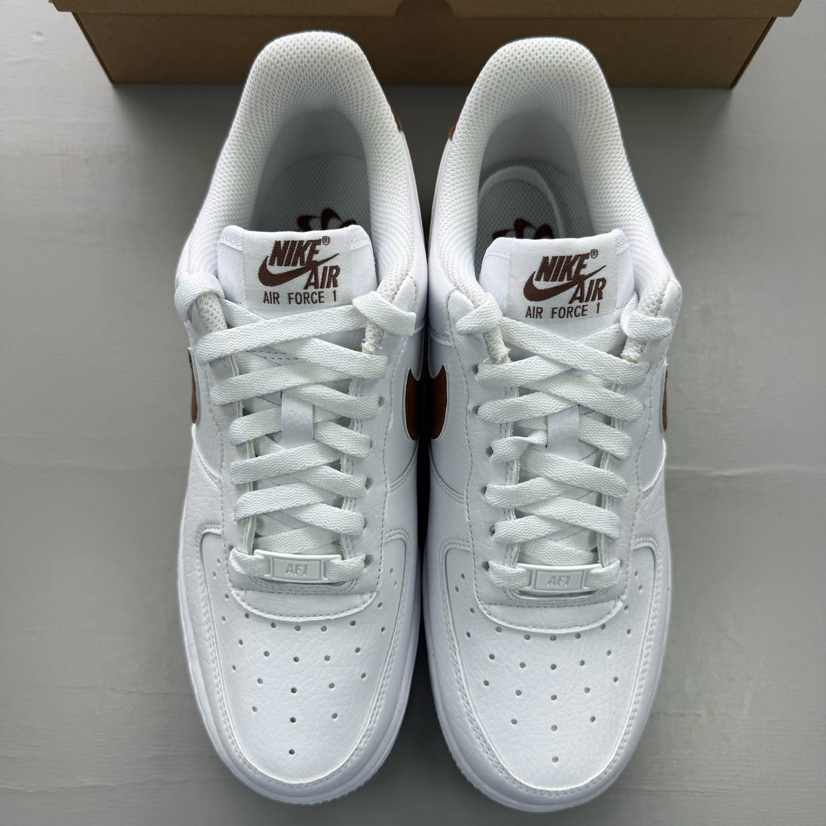 Nike Air Force 1 trainers white with brown accents and signature logo detail.