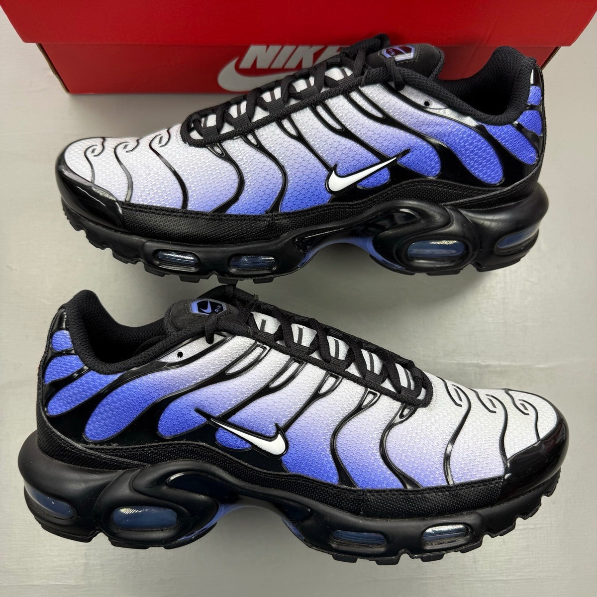 Nike Air Max Plus TN black trainers with sapphire blue accents and signature logo.