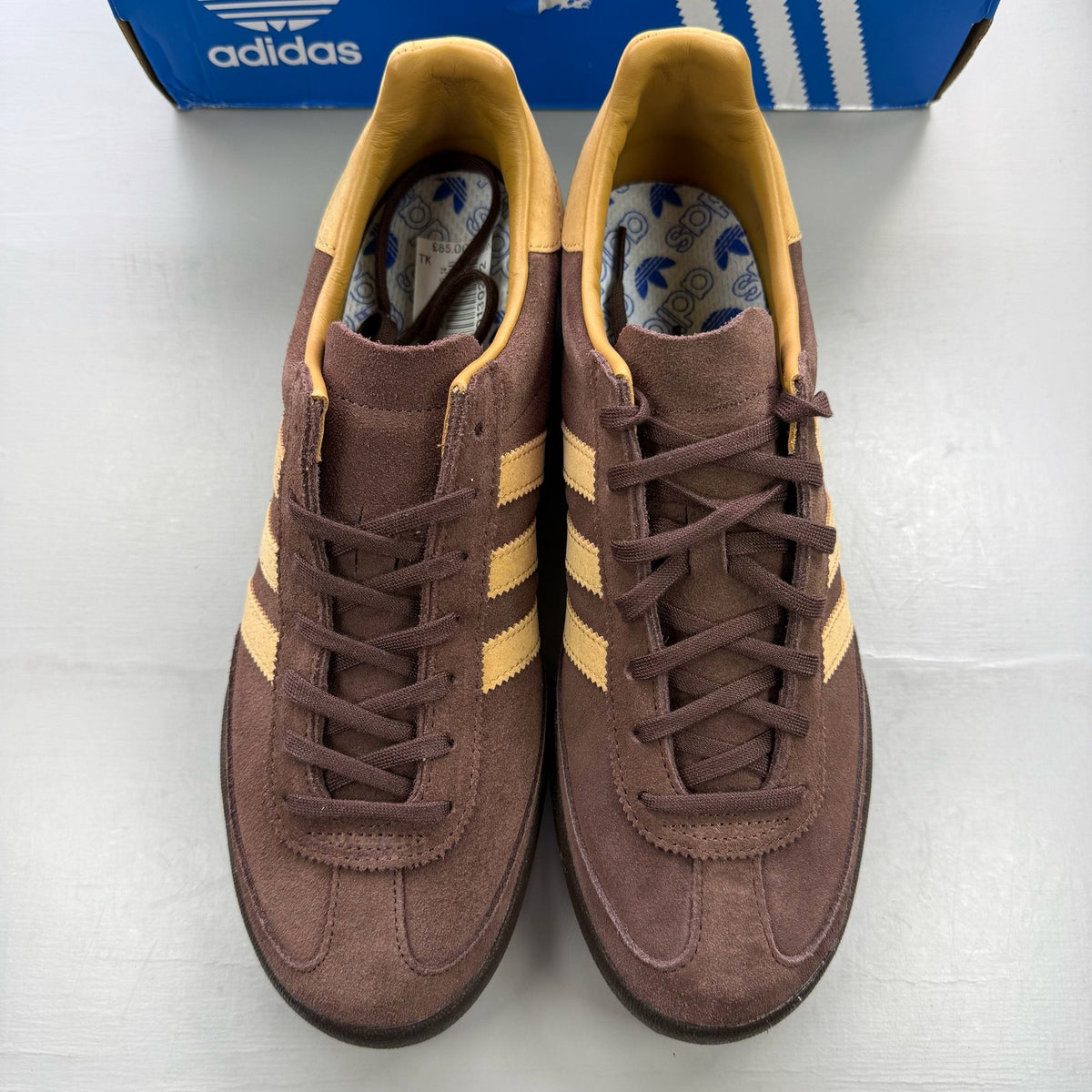 Adidas brown trainers with gold accents and gum sole, featuring iconic three stripes logo.