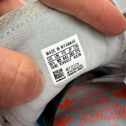 Adidas grey trainers with coral accents and gum sole, featuring classic logo.