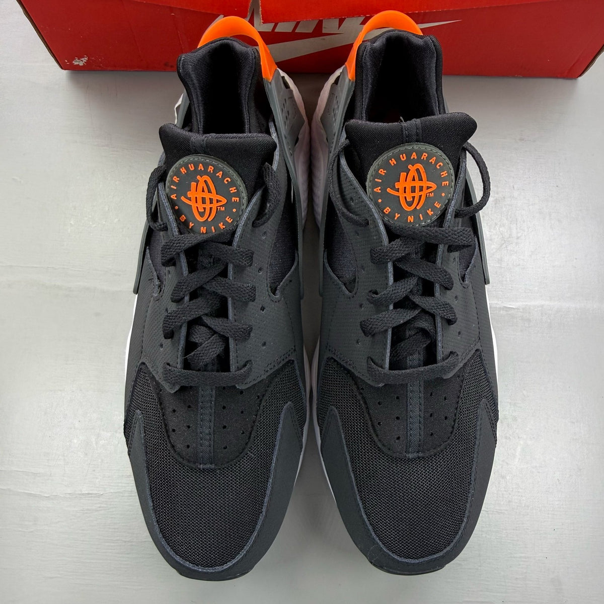 Nike black Air Huarache trainers with safety orange accents and white sole.