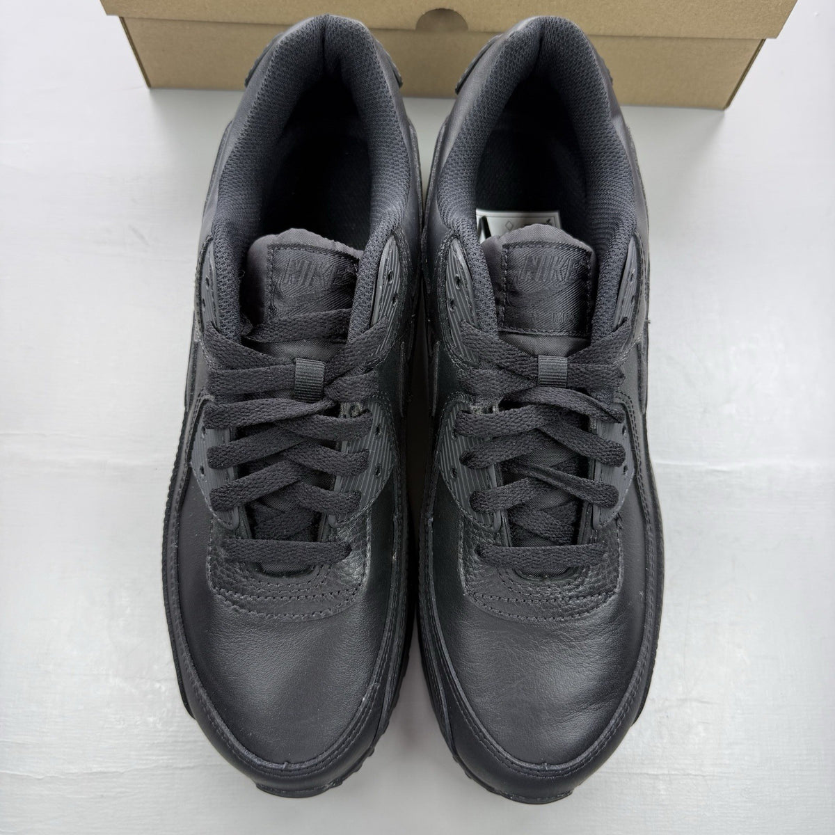 Nike Air Max 90 trainers black leather with signature swoosh logo and textured detailing.