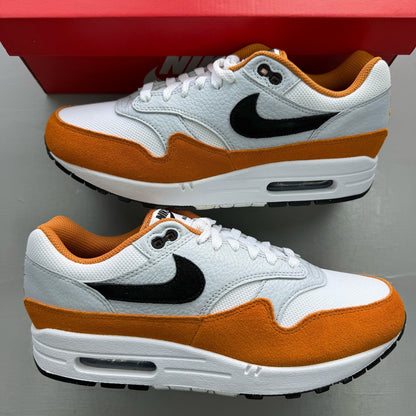 Nike Air Max 1 white trainers with Monarch orange and black accents, featuring logo details.