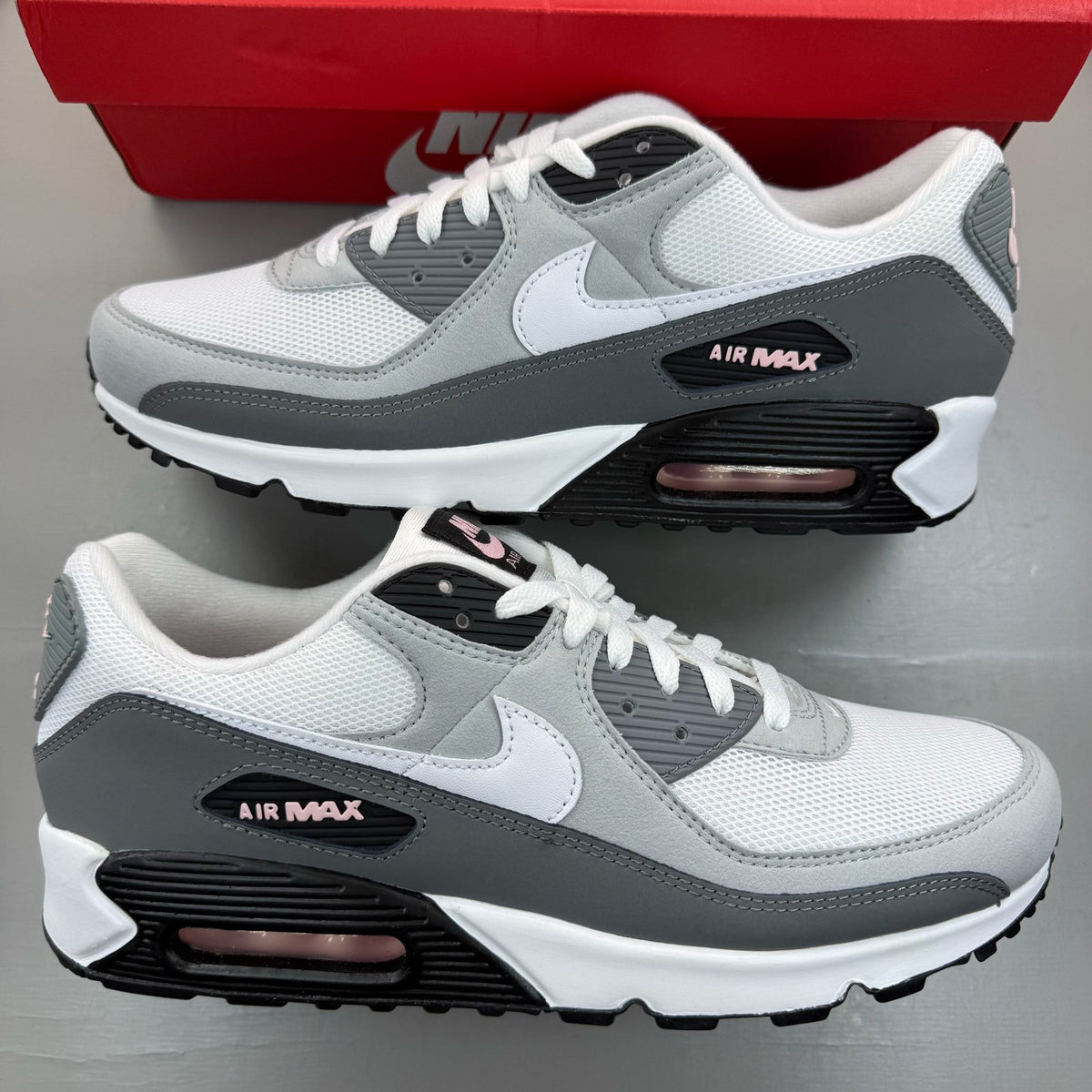 Nike Air Max 90 grey trainers with pink foam accents and white sole.