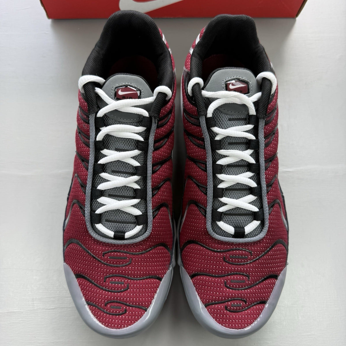 Nike Air Max Plus TN red trainers with grey and black accents, featuring signature logo.