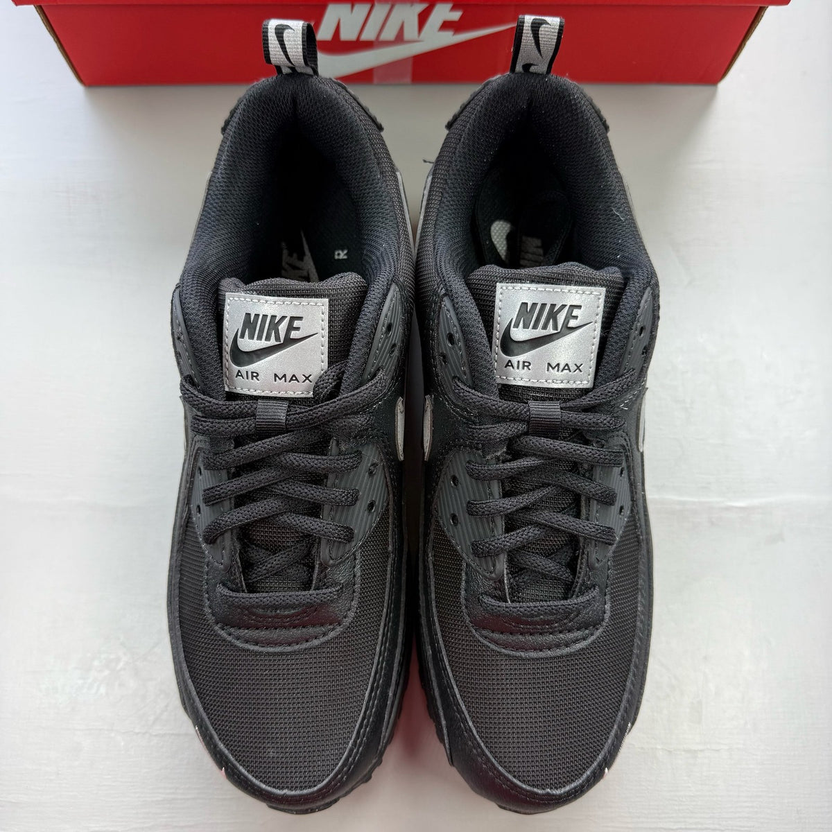 Nike black trainers with metallic silver swoosh logo and sleek design.