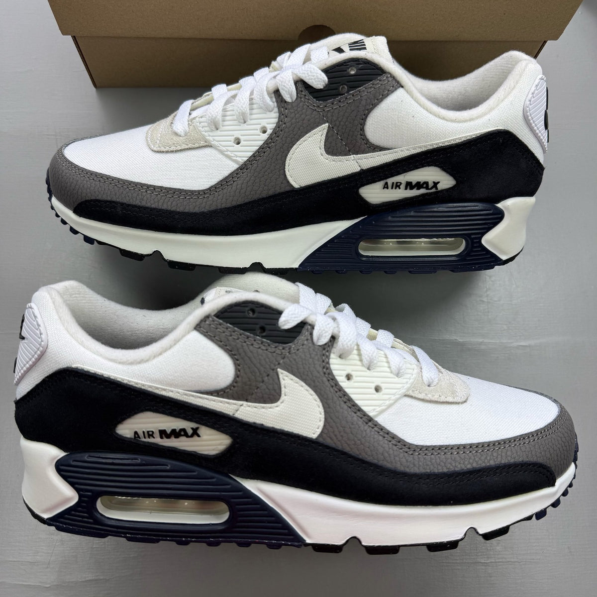 Nike Air Max 90 white trainers with obsidian and pewter accents, featuring logo detail.