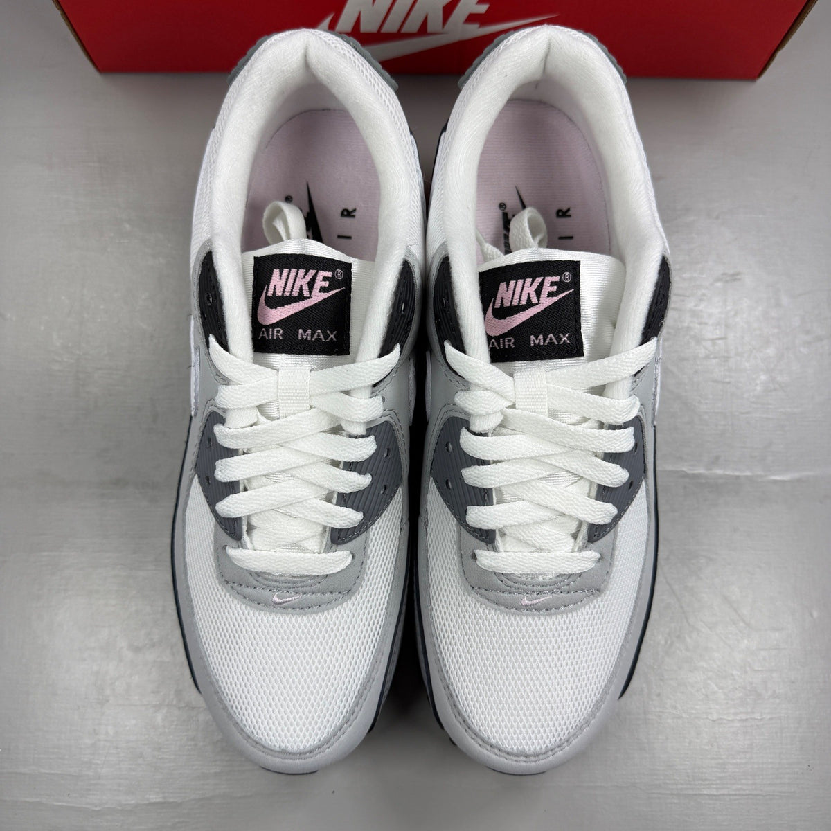 Nike Air Max 90 grey trainers with pink accents and white sole, featuring logo detail.