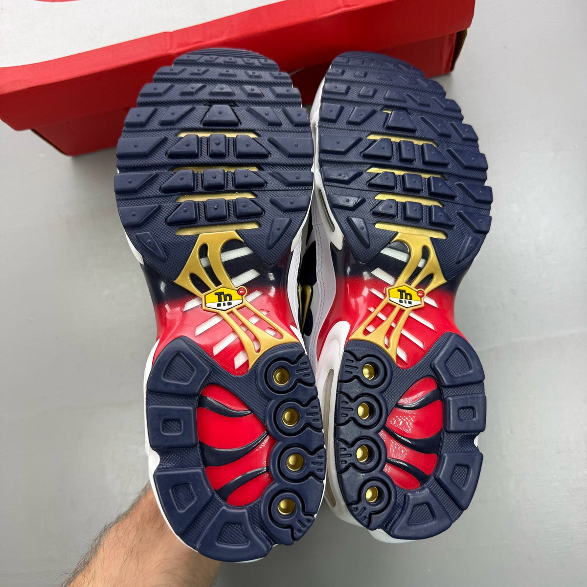 Nike Air Max Plus trainers white with navy and red accents, featuring logo details.