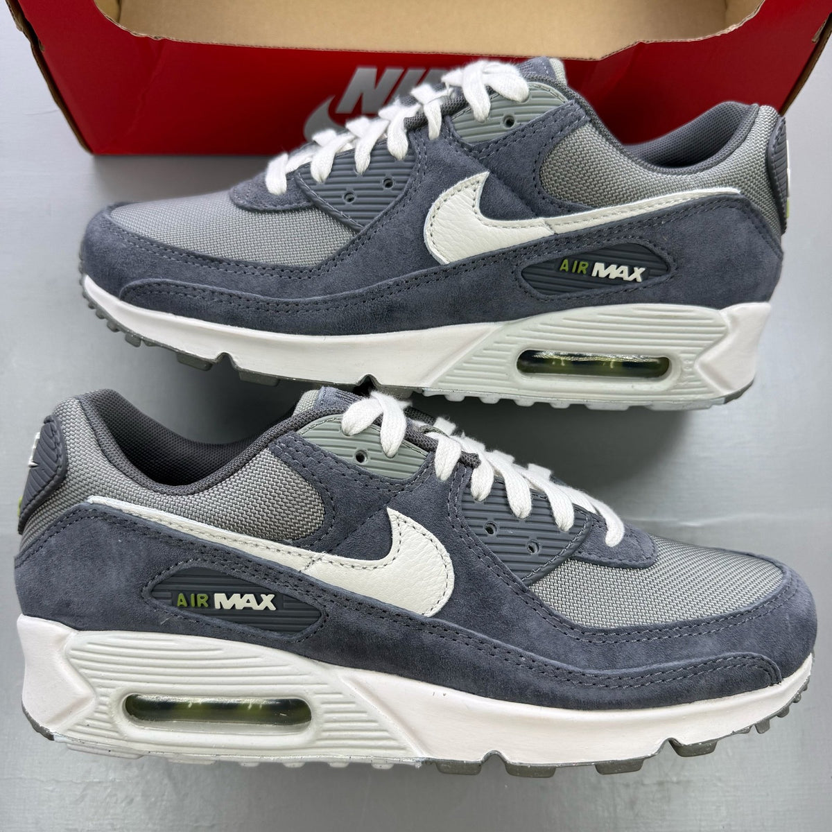 Nike Air Max 90 PRM grey trainers with white accents and distinctive logo details.