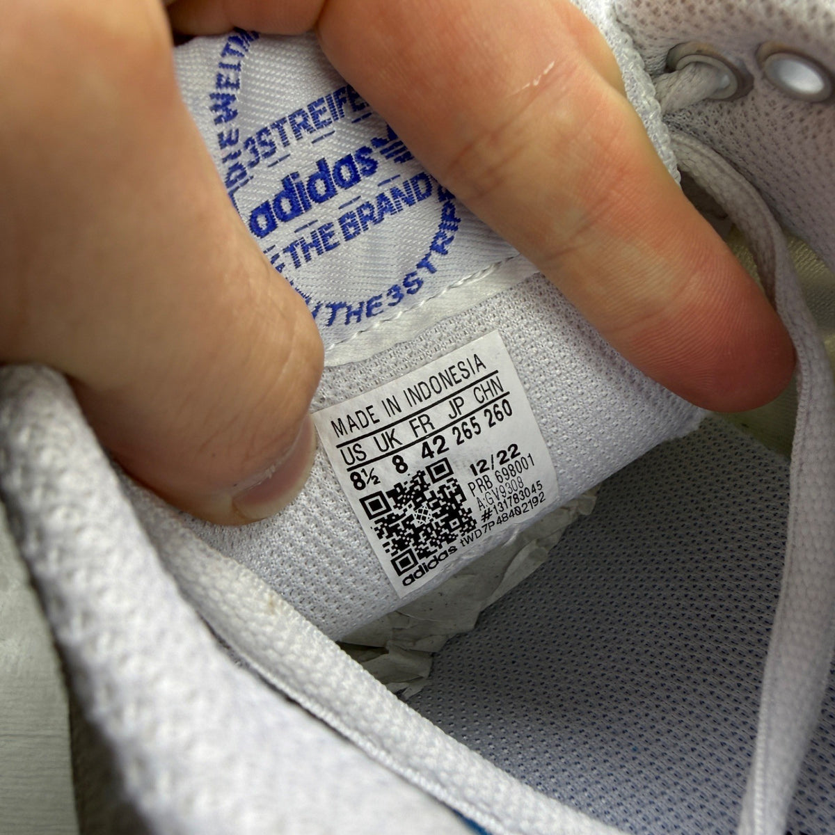 Adidas white trainers with blue accents and woven texture, featuring iconic logo.