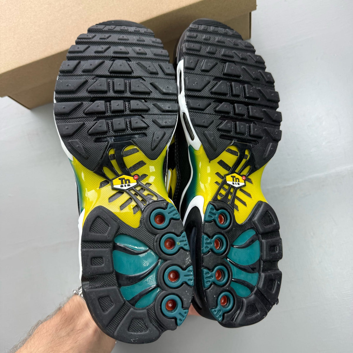Nike Air Max Plus TN black trainers with teal and yellow accents, featuring logo detailing.