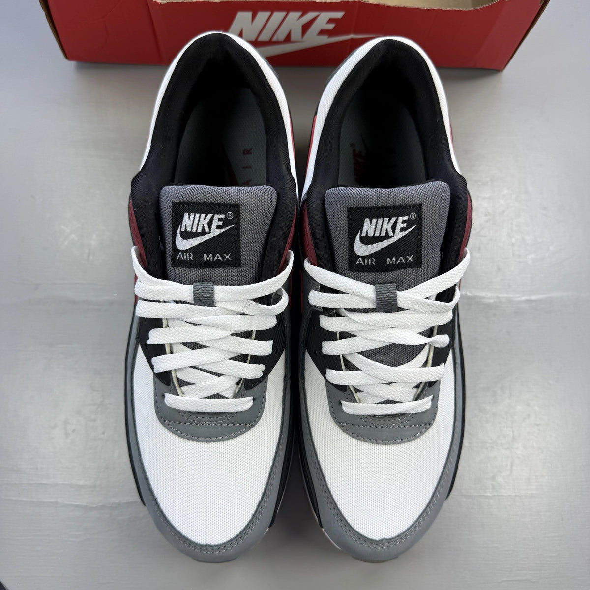 Nike Air Max 90 grey trainers with red accents and gum sole, featuring logo details.