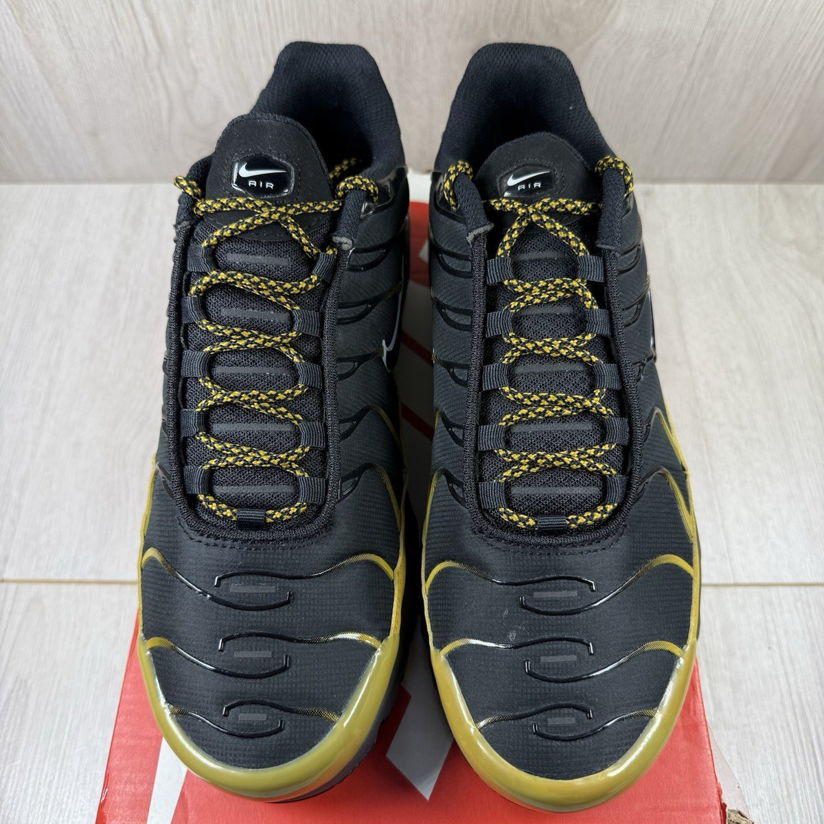 Nike Air Max Plus TN trainers black with gold accents and distinctive wavy pattern.