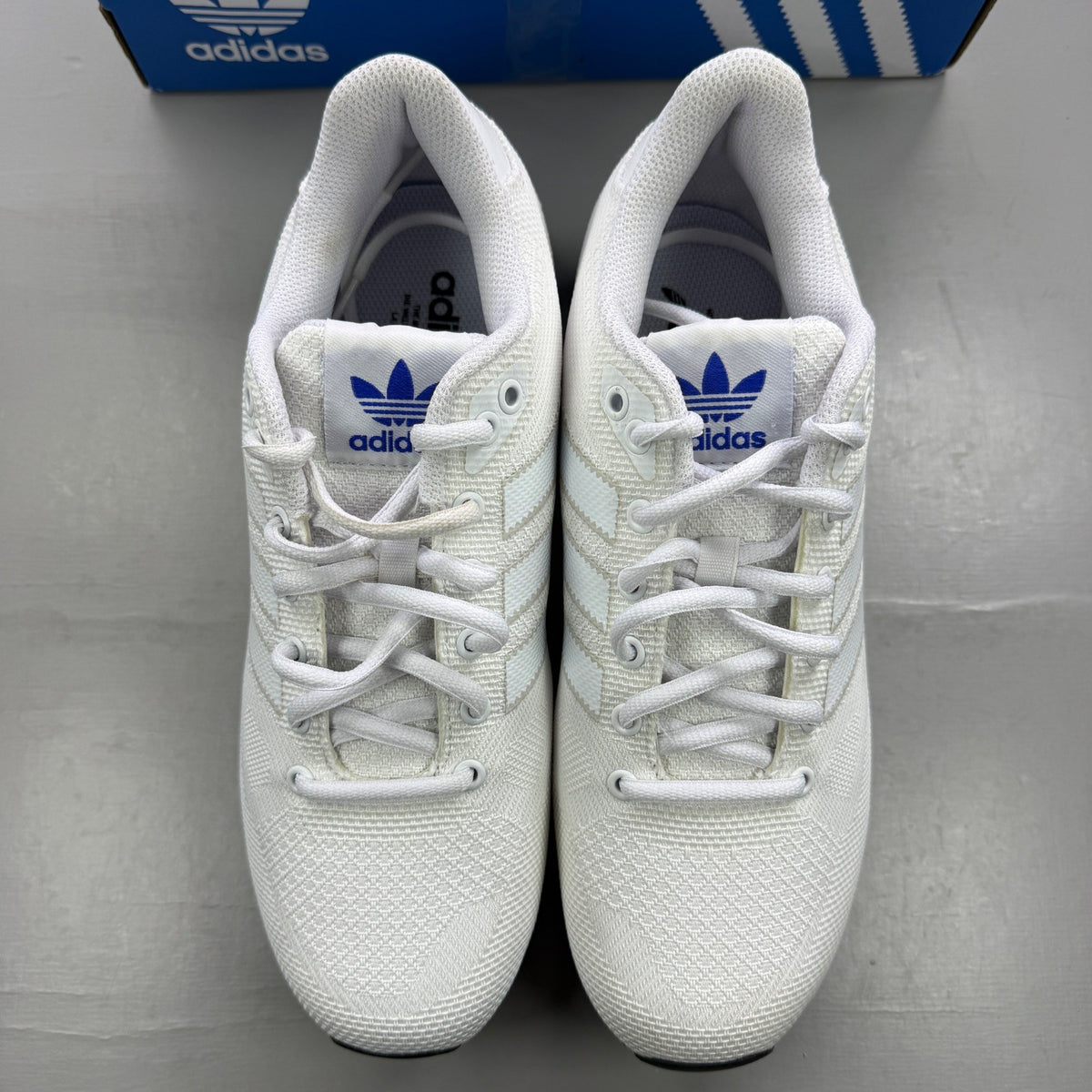 Adidas white trainers with blue accents and woven texture, featuring iconic logo.