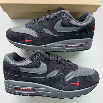 Nike Air Max 1 black trainers with university red accents and logo detail.