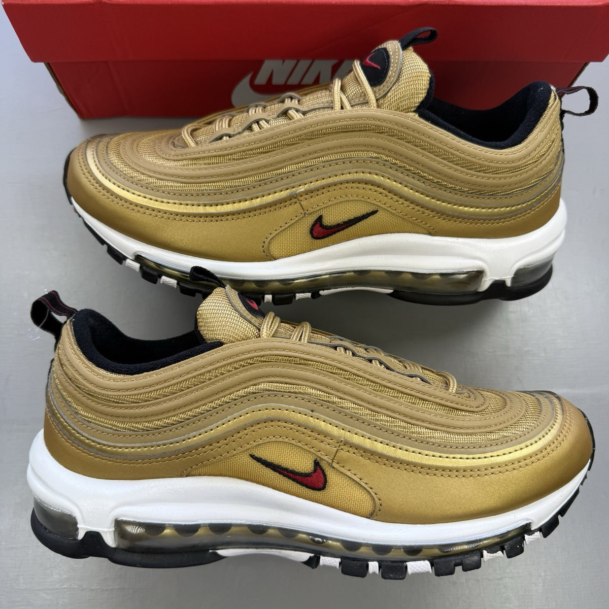 Nike Air Max 97 gold trainers with white and black accents, featuring a sleek design.