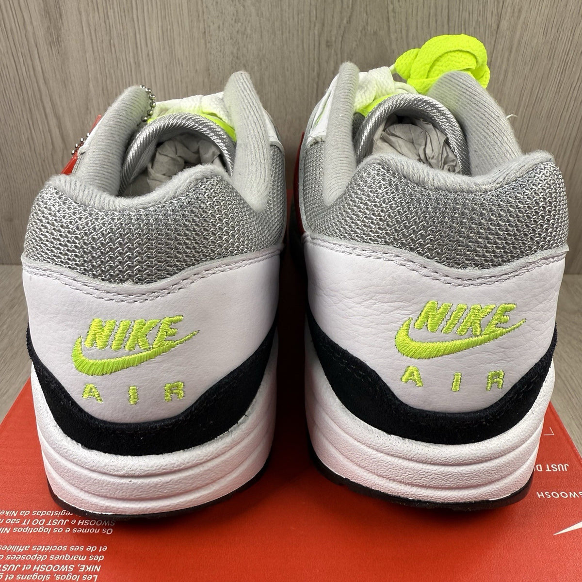 Nike Air Max 1 trainers white with chili volt accents and black detailing.
