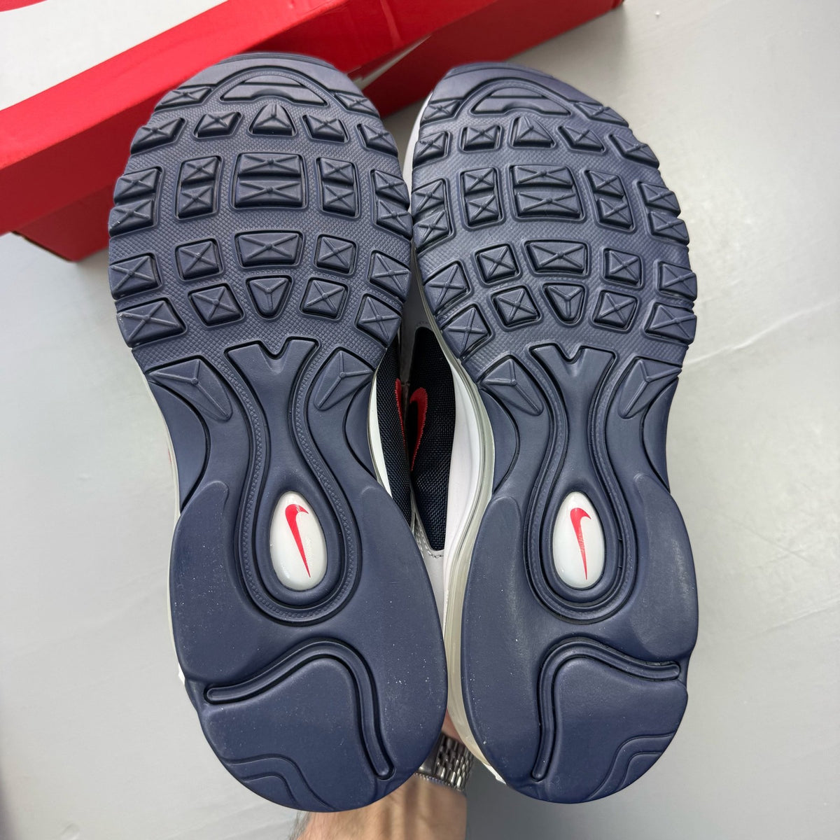 Nike Air Max 97 blue trainers with red accents and iconic logo detailing.